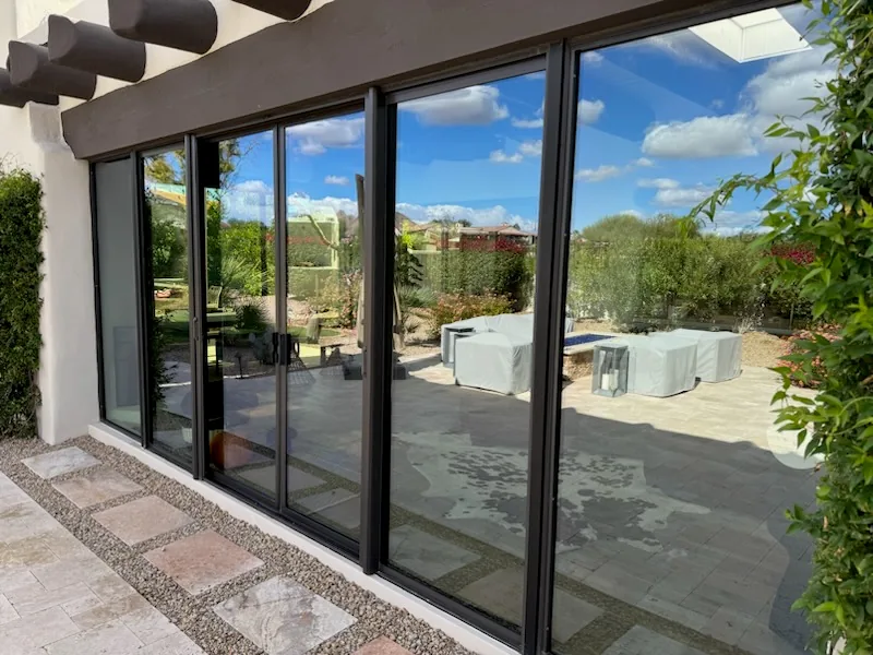 Large black-framed sliding glass doors and windows opening to a patio with desert landscaping.
