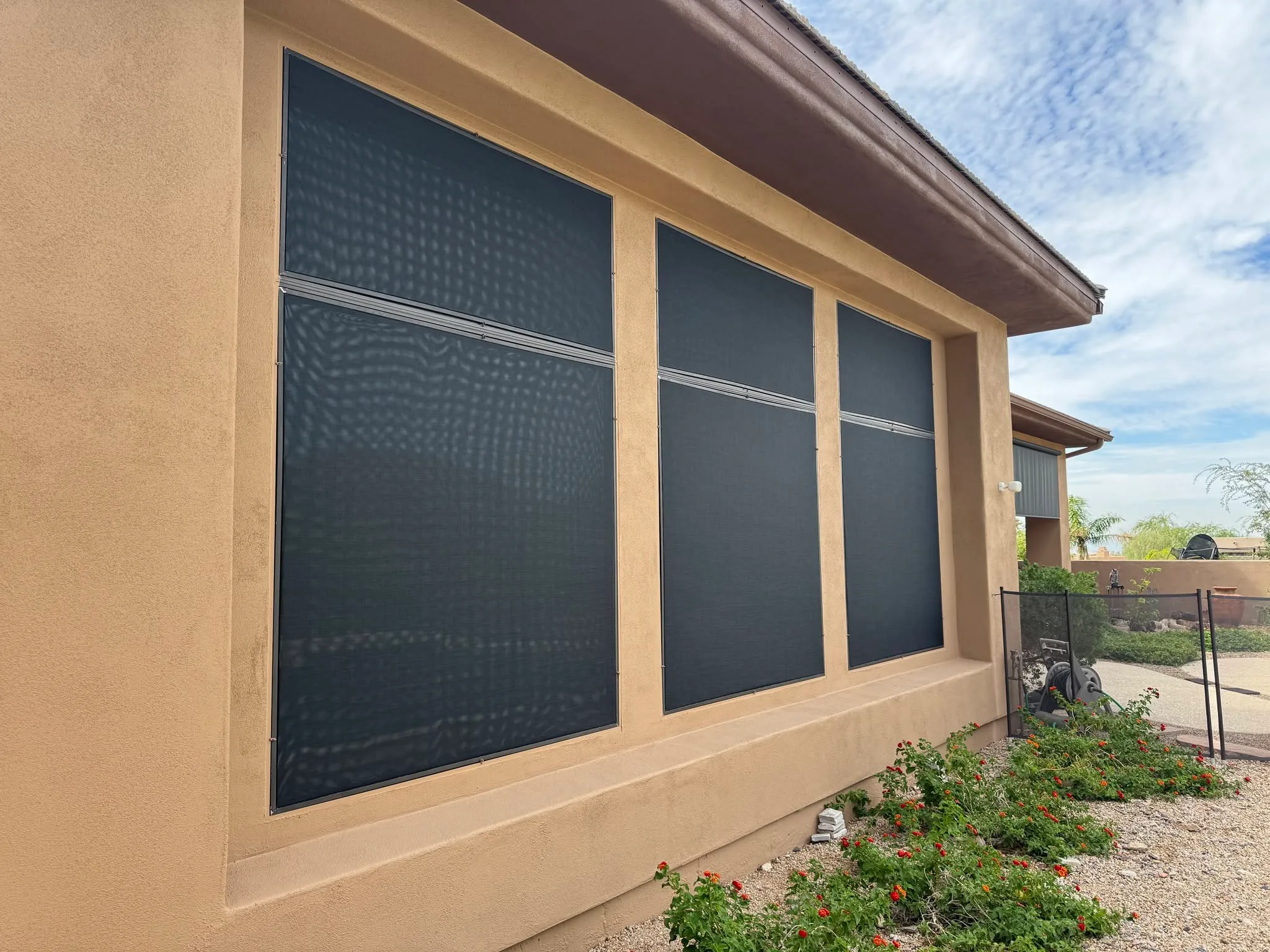 Three large black retractable screens installed on tan stucco building exterior.